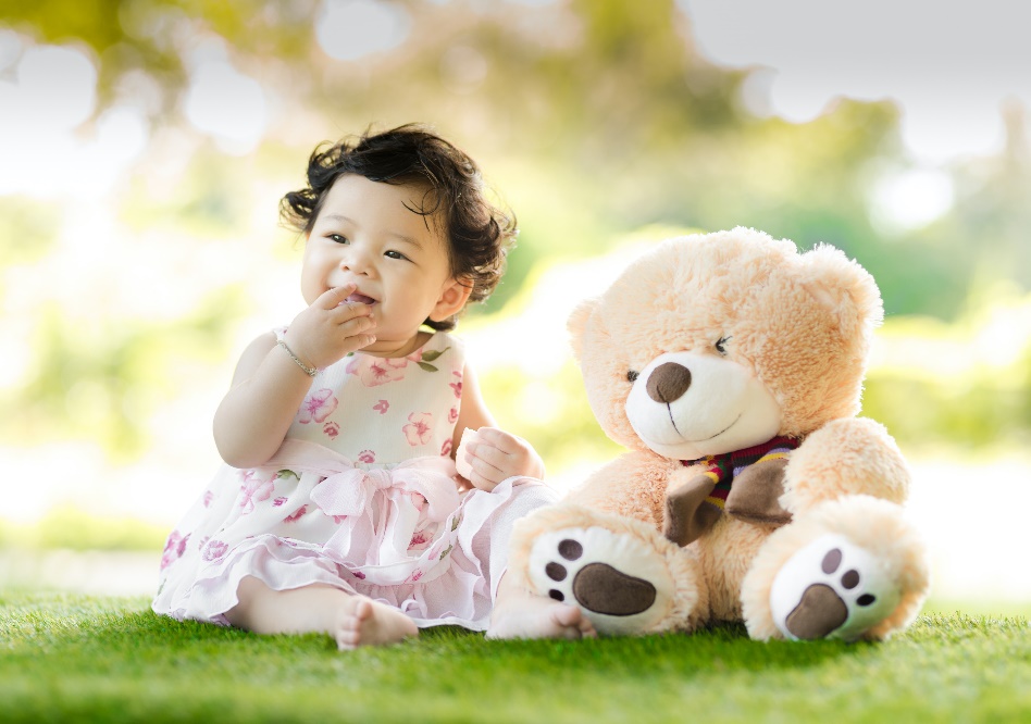 A baby sitting on the grass beside a plush bear toy
