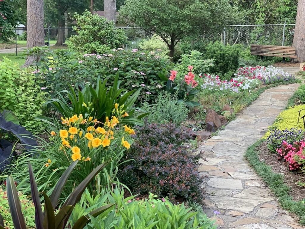 a backyard with a pathway surrounded by plants and flowers